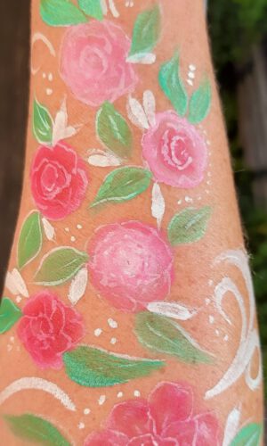 Arm mit mehreren in Pastellfarben gemalten Rosen und grünen Blättern sowie weißen Verzierungen