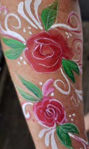 Arm mit zwei rot-rosa Rosen und grünen Blättern sowie weißen und rosa dekorativen Mustern bemalt