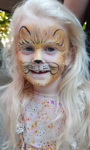 Mädchen mit Löwen-Gesichtsbemalung, lächelnd in einem Blumenkleid