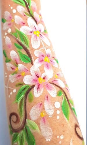 Arm mit bemalten weißen und rosa Blüten, grünen Blättern und braunen Ranken