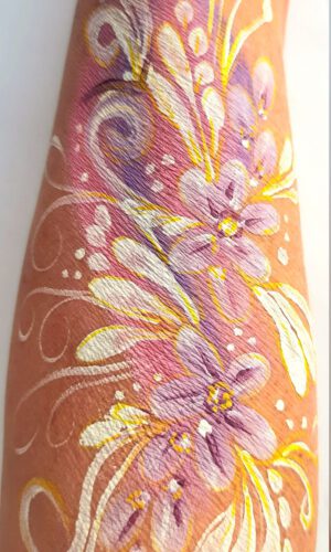 Arm mit floraler Körperbemalung in Weiß und Violett mit geschwungenen Linien und Punkten