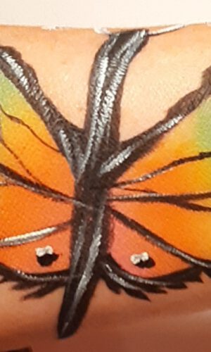 Bunter Schmetterling als Tattoo auf einem Arm mit schwarzen Konturen und weißen Akzenten