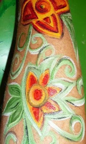 Unterarm mit bunter Körperbemalung aus zwei stilisierten Blumen und grünen Ranken